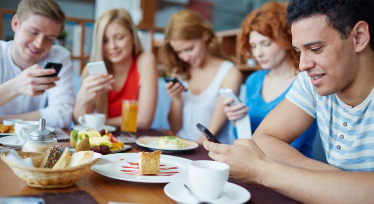 Um grupo de pessoas adultas, sentadas ao redor de uma mesa, mexendo no celular
