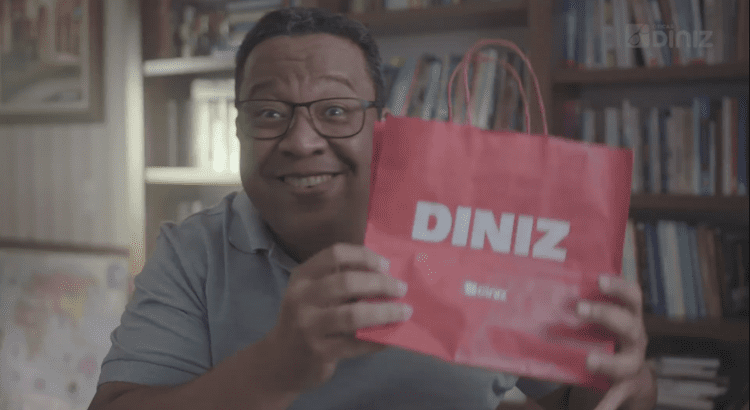 Campanha_Mês dos Pais_Homem usando óculos, sorridente, segura uma sacola das Óticas Diniz