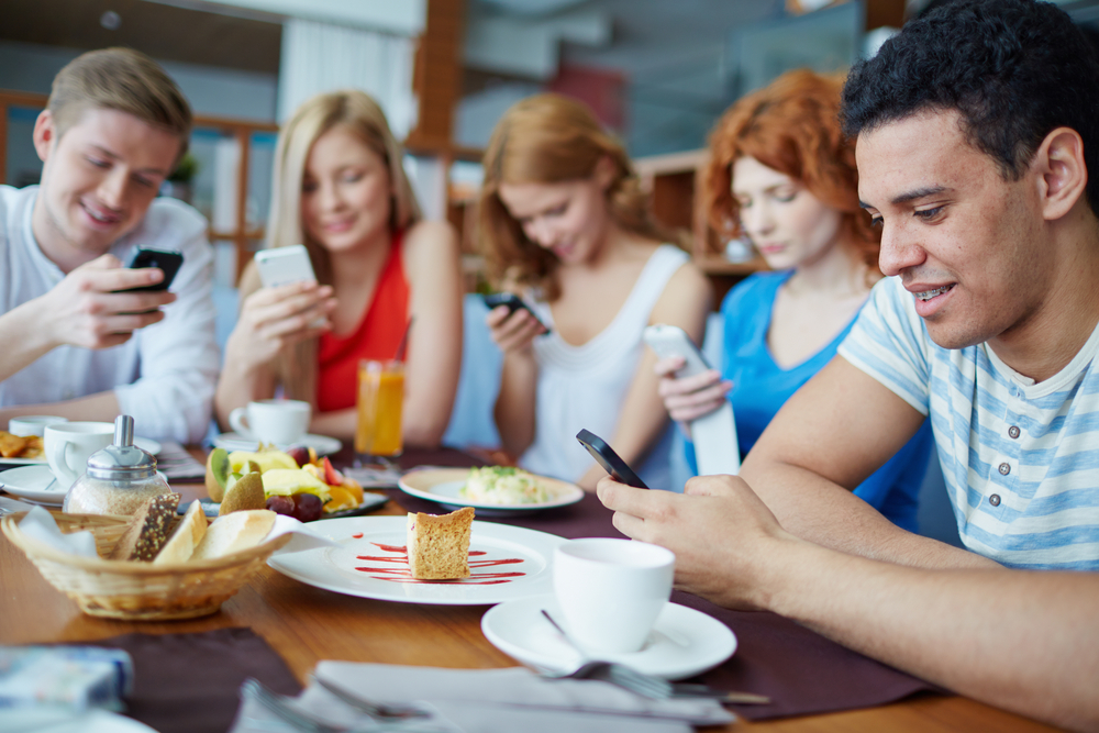 Um grupo de pessoas adultas, sentadas ao redor de uma mesa, mexendo no celular