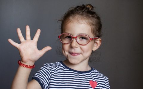 Menina de óculos vermelho com uma das mãos aberta formando o número cinco