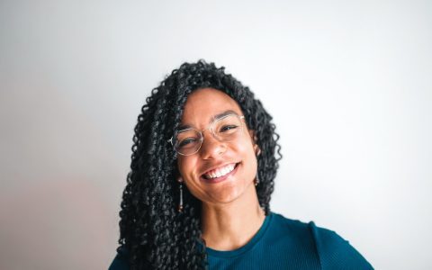 mulher negra, sorri, com seus olhos saudáveis, enquanto usa seus óculos e olha para a câmera ricardo magro