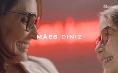 Mulher usando óculos olha, sorridentes para uma menina, que também está de óculos. Celebração do Mês da Mães