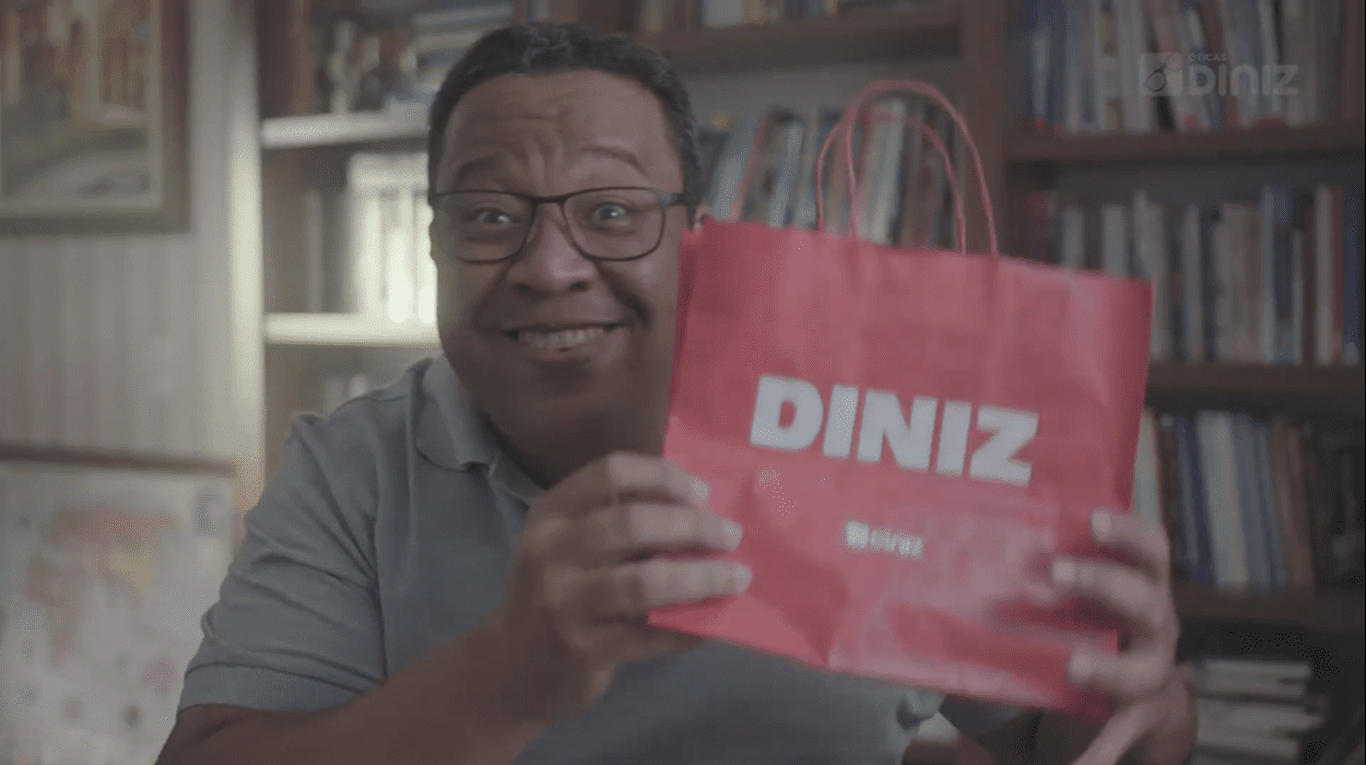 Campanha_Mês dos Pais_Homem usando óculos, sorridente, segura uma sacola das Óticas Diniz