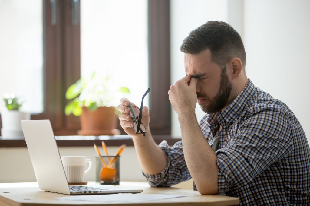 Homem sentado de frente ao computador que aparentar estar com sua visão ruim. Imagem que demonstra os males do colesterol alto