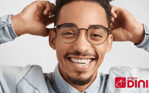 Homem negro e de olhos castanhos usa óculos e sorri, com as mãos na cabeça