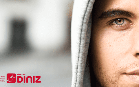 Homem branco, de olhos verdes. Com capuz cinza, posicionado na foto aparecendo metade do rosto