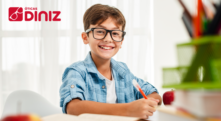 Menino usando óculos contra a miopia infantil sorri enquanto faz sua lição