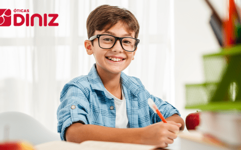 Menino usando óculos contra a miopia infantil sorri enquanto faz sua lição