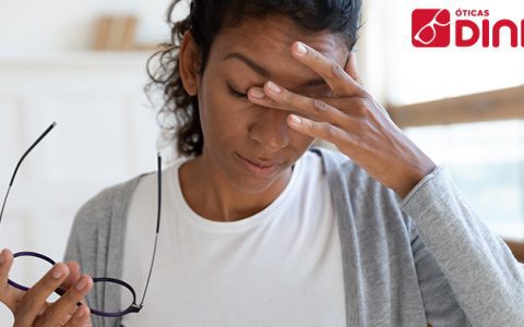 Mulher negra com a vista cansada segura os óculos com a mão direita e coça os olhos com a mão esquerda