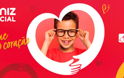 Imagem mostra no centro criança branca com óculos de armação preta e blusa vermelha. à esquerda, há a logo de Diniz Social, hashtag "Enxergue com o coração" e texto "e veja mais esperança". À direita, há o logo das Óticas Diniz.
